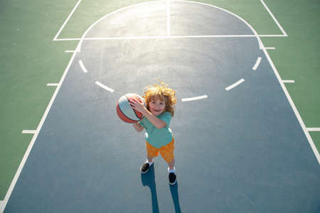 Cute smiling boy plays basketball. Kid shooting basketball ball and playing basketball. Healthy children lifestyle, outdoor on playground.の写真素材