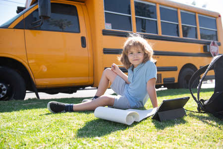 Back to school. Happy child study in park near school bus. Schoolboy doing homework or online education.の写真素材