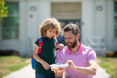 Parent and pupil of primary school schoolboy with backpack. Schoolboy and parent in shirt holding lunch box.の写真素材