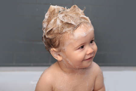 Funny happy baby bathes in bathtub with water and foam. Kids hygiene. Funny kids face close up.