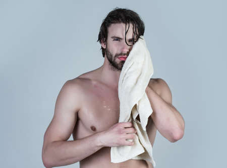 Man in bathroom with muscular body on grey background. Morning washing, wake up, everyday life. Hygiene, sexy guy wash, spa, relax. Man with wet hair hold towel after shower.の写真素材