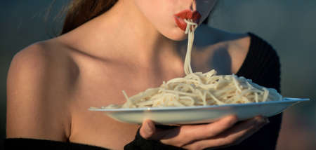Woman with red lips eat pasta. Hunger, appetite, recipe. Sensual lips suck pasta. Italian macaroni or spaghetti for dinner, cook.の写真素材