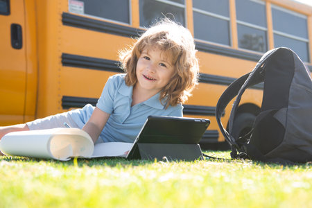 Portrait of smart schoolboy writing outdoor in school park and doing homework.