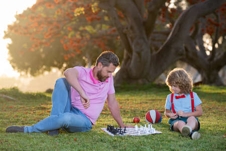Kids chess school. Father and son playing chess lying on grass at lawn park. Fathers Day, love...