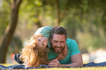 Father and son hugging and embrace on nature in park. Happy dad and child boy enjoying summer time on vacation in a sunny park. Kids love parents affection and tenderness, lovely family.の写真素材
