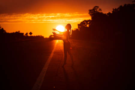 Black silhouette of pretty girl or beautiful woman, sexy slim model, with long hair poses on sea beach at sunset outdoors on yellow sky backgroundの写真素材