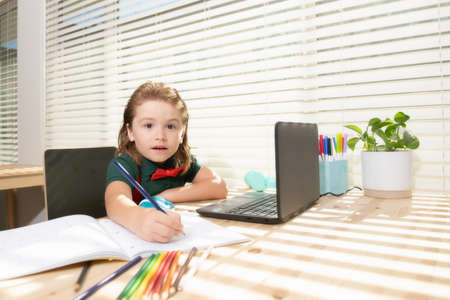 Cute pupil writing at notebook in classroom at the elementary school. Little student doing test in primary school. Children writing notes in classroom during the lessonの写真素材