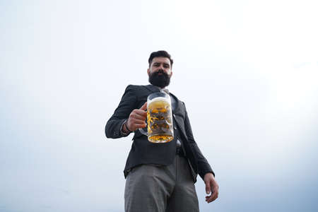 Hipster with beard and mustache in suit drinks beer after working day. Beer time. Handsome barman holding a pint of beer.の写真素材