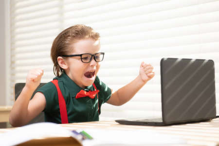 Smart school boy at home writing homework. Little student with notebook computer ready to study. School remote, online learning. Kid at home class learning.の写真素材