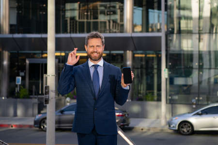 Businessman with phone. Portrait of cheerful Business man office worker talking on mobile phone while standing near modern office.の写真素材