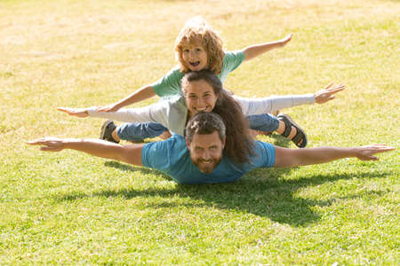 Family lying on grass in park. Fly concept, little boy is sitting pickaback while imitating the flight.の写真素材