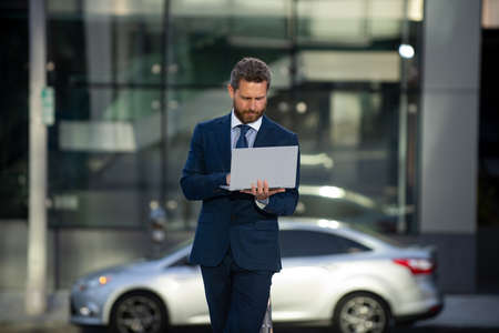 Business man holding laptop standing on the street near business office building.の写真素材