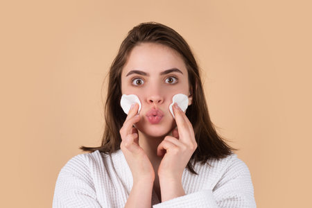 Pretty young girl with daily morning skincare procedures, cleansing face skin with natural lotion tonic using cotton disc sponge pad. Beautiful girl model with natural makeup.の写真素材