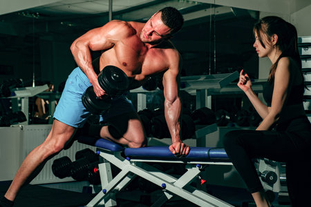 Trainer dumbbell exercises. Boodybuilder couple. Personal friend helping woman working with heavy dumbbells in gym. Sportsman concept. Sport woman.の写真素材