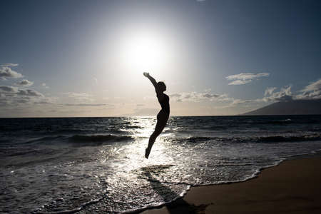Carefree woman with raised hands jumping against sea ocean view and blue sky. Concept of summer sea vacation, travel and freedom.の写真素材