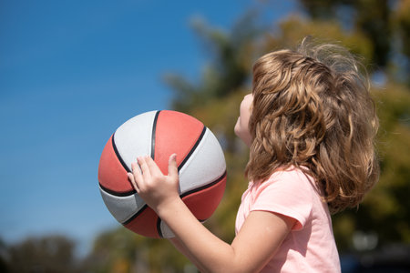 Little caucasian sports kid playing basketball holding ball with happy face. Active kids lifestyle.の写真素材