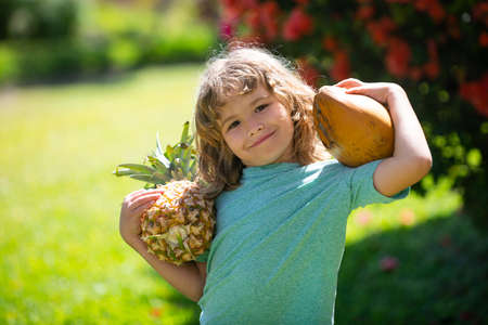 Cute kid with pineapple and coconut at tropical garden. Fresh tropical fruits for kids. Healthy lifestyle with fresh organic tropical fruits.の写真素材