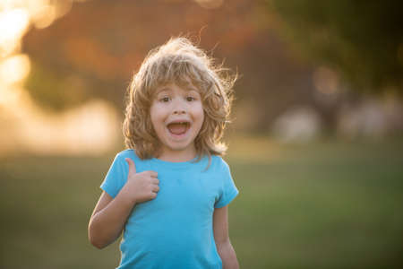 Portrait of a happy laughing child summer outdoor. Close up positive kids face. Thumbs up. Amazed...