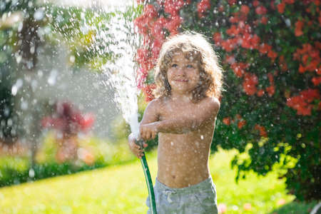 Kid having fun in domestic garden. Child hold watering garden hose. Active outdoors games for kids in the backyard during harvest time.の写真素材