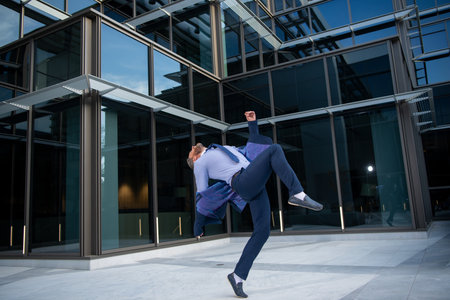 Excited businessman keeping arms raised and expressing positivity while standing outdoors with office building.の写真素材