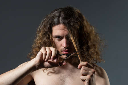 Young sexy man, portrait of guy with barber scissors cut long hair. Modern barbershop, shaving. Handsome male with modern hairstyle on black.の写真素材