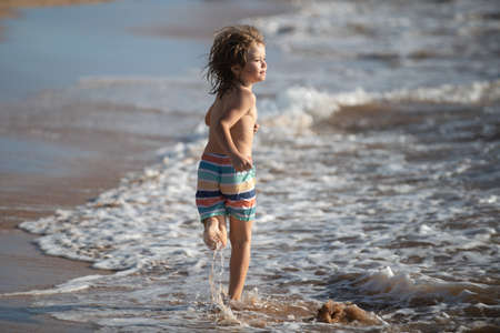 Little boy running on beach shore splashing water in blue sea. Kid walking the summer beach.の写真素材