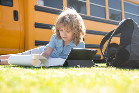 Cute schoolboy laying on grass in the park near school bus. School kid outdoor.の写真素材
