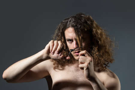 Young sexy man, portrait of guy with barber scissors cut long curly hair for barber shop. Modern barbershop, shaving. Handsome male with modern hairstyle on black.の写真素材