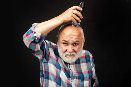 Old man with hair clipper isolated on black. Bald man hairclipper, Mature baldness and hair loss concept.の写真素材
