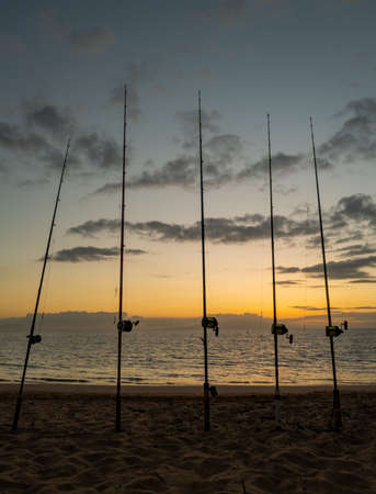 Colorful sunset with fishing rod on ocean. Silhouette of people and fishing rods.の写真素材