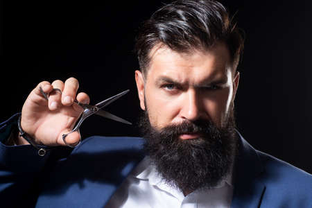Closeup bearded man, portrait of man with long beard and moustache. Barber scissors for barber shop. Vintage barbershop, shaving. Brutal serious male with modern hairstyle on black.の写真素材