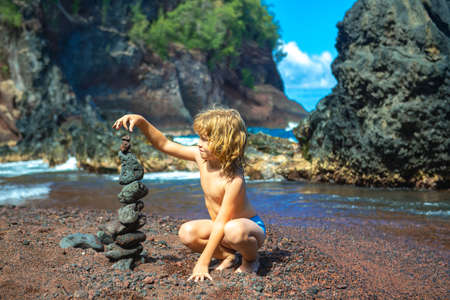 Kid builds a cairn of stones on the sea coast. Beach games with children. Leisure in the evening on vacation with kids. Balance development building fantasy. Childhood. Ocean kids trawel.の写真素材