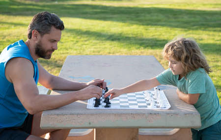 Father and son playing chess spending time together in park. Child playing board game with parent....