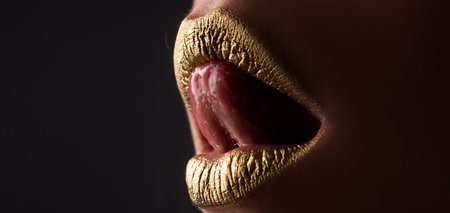 Gold lips. Woman wouth close up with golden color lipstick on lip. Glitter glossy lips biting.の写真素材