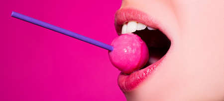 Licking candy. Lollipop model. Woman lips sucking a candy. Glamor sensual model with red lips eat sweats lolly pop isolated on pink.の写真素材