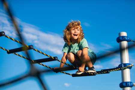 Cute boy climbs up the ladder on the playground. Child climbs up the ladder against the blue sky. Copy space for text.の写真素材