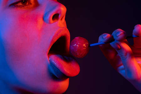 Seduction woman licking lollipop, art banner, red lips with lollipop. Sexy red female mouth and tongue with lolli pop. Art print for design on neon lights. Night club background.の写真素材