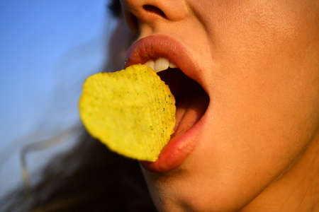 Female mouth eat potato chips. Chips with teeth, tongue and lips close up. Tasty delicious fast food. Eating crisps. Fast food.の写真素材