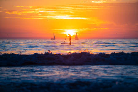 Man paddle boarding during a beautiful sunrise. Sunset at the sea. Sunrise at beach. Colorful ocean...