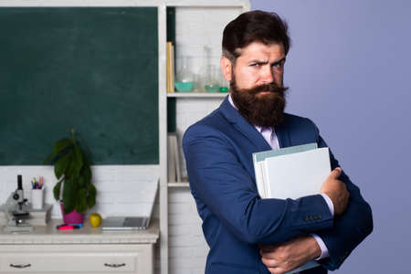 Confident middle-aged male teacher or professor standing in front of a chalkboard with books folded arms.の写真素材