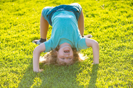 Happy kid boy girl standing upside down on her head on grass in summer day.の写真素材