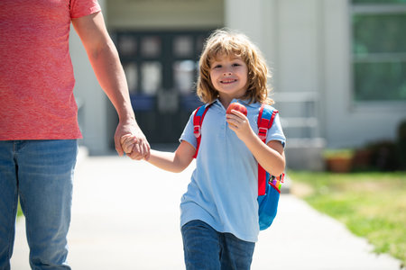 American father and son walking trough school park. First day at school. Father leads a little child school girl in first grade.の写真素材