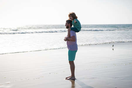 Dad and child walking together on summer beach. Little boy kid with daddy carrying him on shoulders. Dad and child enjoying outdoor. Lifestyle and family vacation, happiness men concept.の写真素材