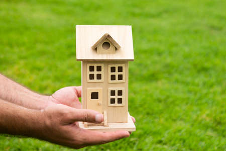 Hand holding model of house close up. Small miniature toy house. Mortgage property insurance dream moving home and real estate concept.の写真素材