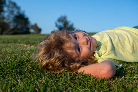 Portrait of a happy little boy laying on the grass in the park. Outdoor portrait of pretty little boy on fresh green grass. Summer fun, happy childhood.の写真素材