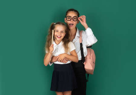 Knowledge day, Smiling funny little schoolkids sisters girls with backpack hold books on green blackboard. Childhood lifestyle concept. Education in school.の写真素材