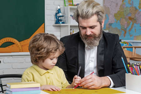 Father teaching son. Funny little child with father having fun on blackboard background. Supporting pupils at school. Private kids tutoring.の写真素材