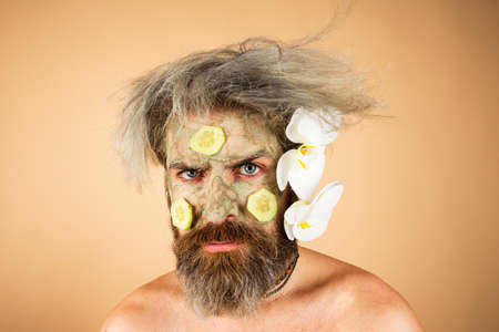 Funny man with clay mask and cucumber slices on face. Male spa, dermatology, wellness and facial treatment concept.の写真素材