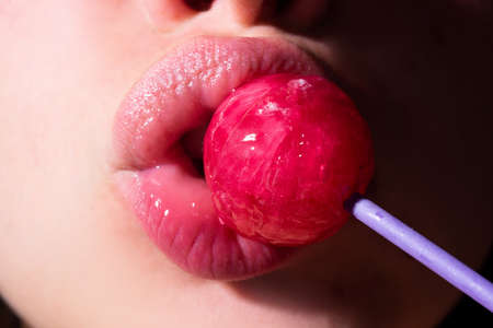 Sexy woman mouth with pink lips holding lollipop, beauty closeup. Sexy girl suck lick lollipop. Beauty glamour concept, close-up.の写真素材