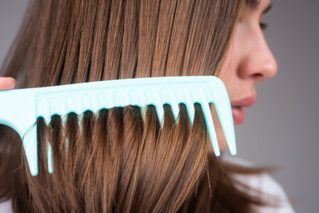 Close up brunette hair lady combing hair with hairbrush comb, isolated. Long healthy brunette hair,...